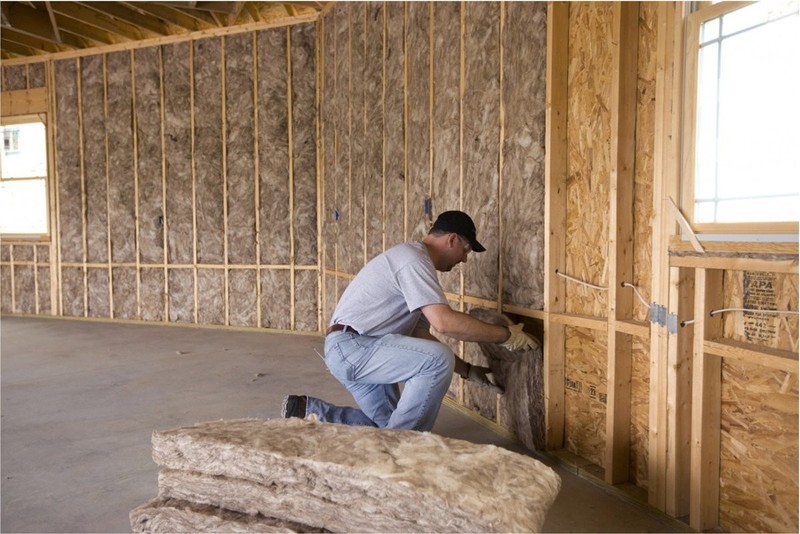 Pracownik izoluje pianką ściany domu szkieletowego
